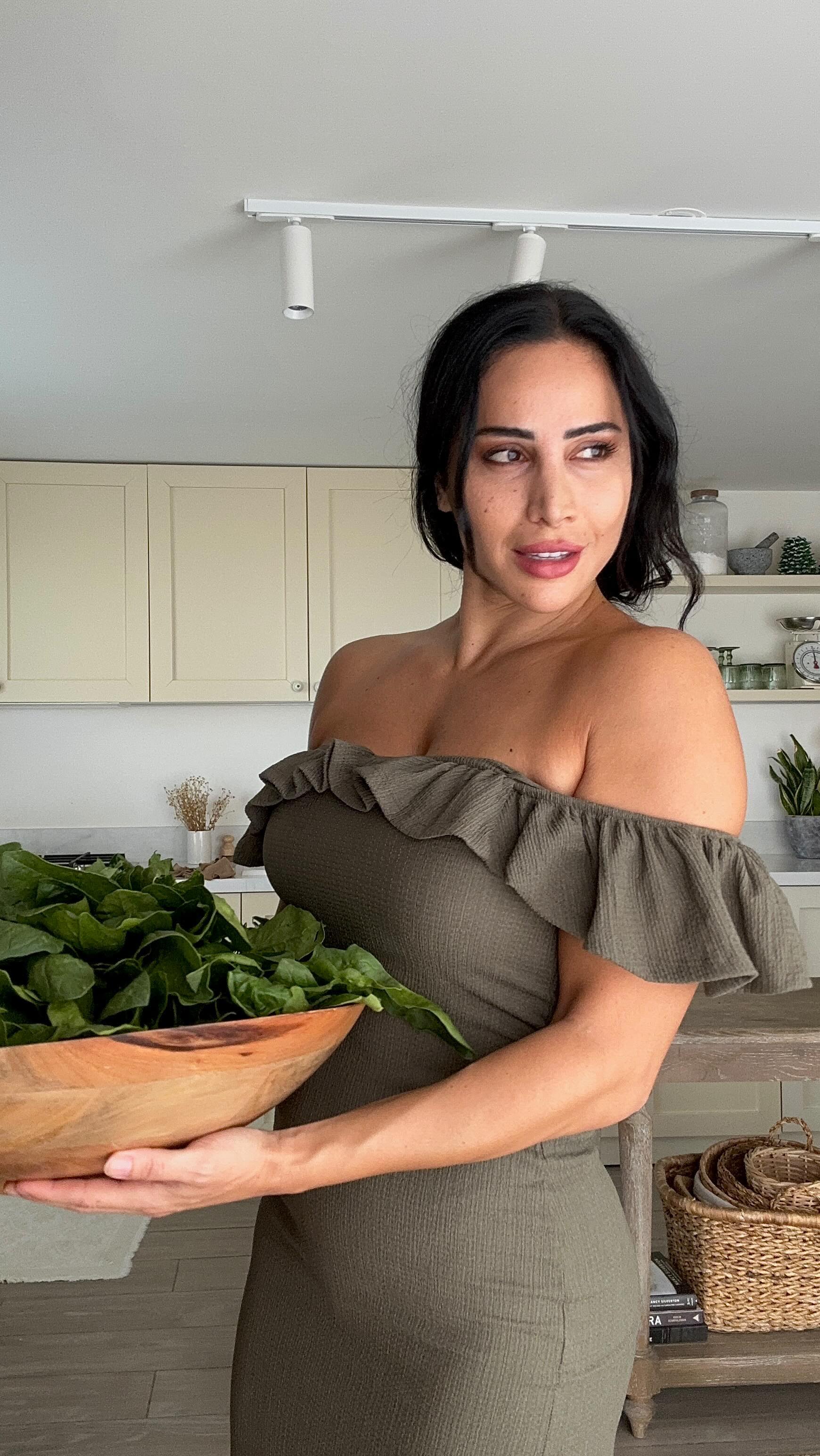 Rana in her kitchen holding a wooden bowl of fresh greens